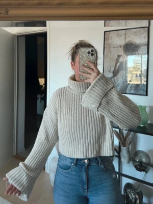 Beige stickad polotröja med vida ärmar - Säljer en beige stickad polotröja med bred ribbstickning och extra vida ärmar. Tröjan har hög krage och är något croppad i modellen. Perfekt för dig som gillar en avslappnad och trendig stil.
