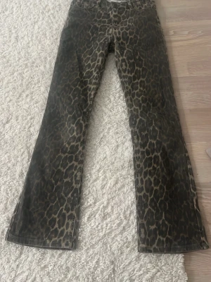 Leopardmönstrade bootcut jeans - Säljer ett par riktigt snygga leopardmönstrade jeans med bootcut passform. Jeansen har en cool brun och svart färgkombination och är tillverkade i ett klassiskt denimtyg. Perfekta för dig som vill sticka ut och addera lite edge till din outfit.