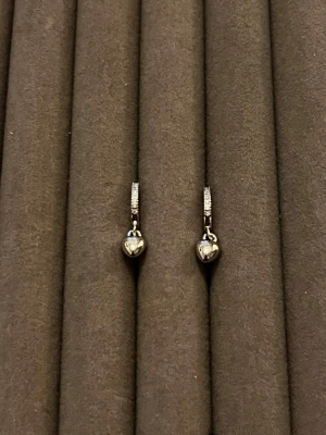 Silverörhängen med hjärtberlocker - Snygga örhängen i silverfärg med små hjärtformade berlocker. Örhängena har en tunn båge dekorerad med gnistrande stenar som ger extra bling. Perfekta för dig som gillar stilrena men ändå iögonfallande accessoarer. Materialet ser ut att vara metall med stenar.