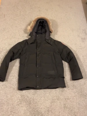 Svart dunjacka med pälskantad huva - Snygg svart dunjacka med stor huva och pälskant. Jackan har flera stora fickor framtill, quiltad design och stängs med både dragkedja och knappar. Perfekt för kalla vinterdagar och har en klassisk, rak passform.