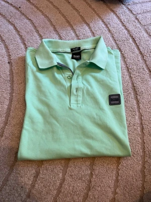 Mintgrön pikétröja från BOSS - Snygg mintgrön pikétröja från BOSS med klassisk krage och knappar framtill. Tröjan har en diskret logotyp på bröstet och är tillverkad i mjuk bomull som känns skön mot huden. Perfekt för en avslappnad men stilren look. Använd gärna köp nu