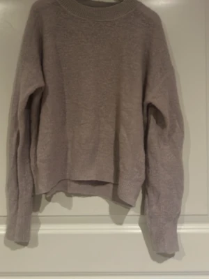 Ljuslila/rosa stickad tröja - Mysig ljuslila stickad tröja med rund halsringning och långa ärmar. Tröjan har ribbade muddar vid hals, ärmslut och nederkant. Perfekt för lager på lager och enkel att matcha med jeans eller kjol.