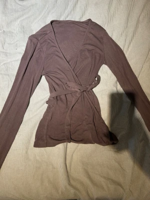 Vintage kofta  - Snygg brun vintage tröja med långa ärmar och knytband i midjan. Koftan har en smickrande passform och är tillverkad i ett mjukt, tunt material som känns skönt mot huden. Perfekt att slänga över en topp för en avslappnad look.