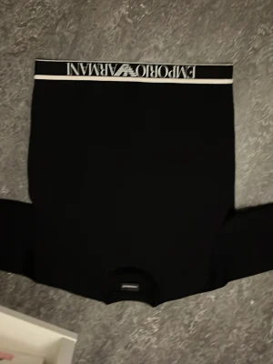Svart sweatshirt Emporio Armani - Svart sweatshirt från Emporio Armani med vit logga och text längs nederkanten. Tröjan har rund halsringning, långa ärmar och ribbade muddar. Tillverkad i mjukt material för en clean och stilren look.