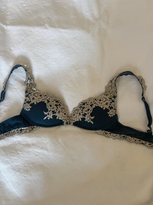 Intimissimi bh - Säljer en mörkblå bh med vacker beige spets och blommig brodyr. Bh:n har vadderade kupor och justerbara axelband. Materialet är en kombination av mjuk mesh och spets som ger en lyxig känsla. Perfekt för dig som gillar detaljer och romantisk stil. 80b