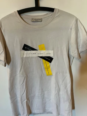 Vit Givenchy t-shirt med tryck - Säljer en vit t-shirt från Givenchy med coolt grafiskt tryck i svart, vitt och gult framtill. Klassisk rund hals och korta ärmar. Perfekt för dig som gillar exklusiva streetwear-vibbar och vill sticka ut lite extra.