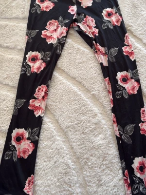 Blommiga leggings från Divided - Snygga leggings från Divided med svart bas och stora rosa blommor. Tillverkade i stretchigt material av polyester och elastan för skön passform. Perfekta för dig som vill ha ett statement-plagg med coolt mönster och bekväm känsla.