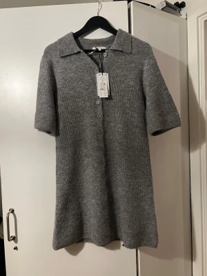 Grå stickad klänning med knappar - Mysig grå stickad klänning med kort ärm och knappar hela vägen framtill.  Endast testad , kan lukta parfym