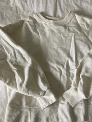 Vit sweatshirt - En basic vit sweatshirt i mjukt bomullsmaterial med rund halsringning och ribbade muddar vid ärmar och midja. Perfekt för en clean och avslappnad stil. Passar till det mesta och är enkel att matcha.