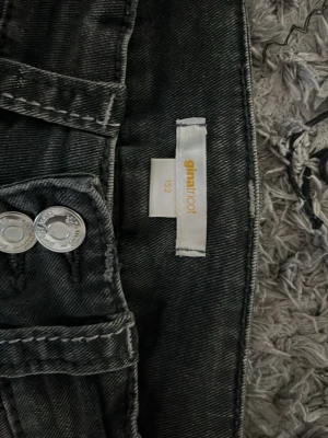 Svarta jeans från Gina Tricot - Säljer ett par svarta jeans från Gina Tricot med dubbla silverknappar och vita kontrastsömmar. Klassisk femficksmodell med snygg tvätt och normal midja. Perfekta till vardagslooken och lätta att matcha med olika stilar.