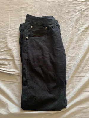 Svarta slim fit jeans - Säljer ett par svarta slim fit jeans med klassisk femficksdesign och silverfärgade nitar. Jeansen har en enkel look utan slitningar och är tillverkade i ett mjukt denimtyg som ger en skön passform. Perfekta till en avslappnad streetstyle.