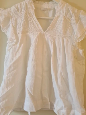 Vit blus med spetsdetaljer - Söt vit blus i tunn, 100% bomull med v-ringning och korta ärmar. Blusen har fina spetsdetaljer samt volangkantade ärmar. Perfekt för en somrig och avslappnad look. Är köpt på gina tricot young i storlek 158/164 men passar skulle säga att den passar XS. Aldrig använd