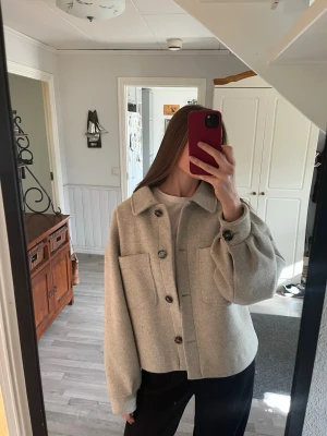 Ljusgrå jacka/overshirt från NA-KD - Ljusgrå jacka/overshirt från NA-KD med stora framfickor och knappar framtill. Overshirten har en rak, boxig passform och klassisk krage. Materialet har blivit noppigt.