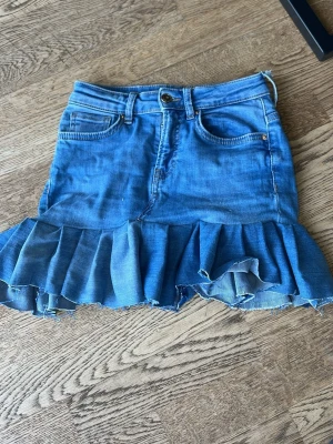 Blå jeanskjol med volang från jeans från Only - Säljer en blå jeanskjol, som jag sytt själv, den är gjord av jeans från Only med volangkant nedtill och klassiska fickor fram och bak. Kjolen har en söt broderad hjärtdetalj på ena bakfickan och råa kanter för en trendig look. Perfekt för dig som gillar denim och vill ha något extra.