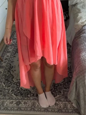 Korallrosa omlottklänning - Säljer en korallrosa klänning med v-ringning och omlottdetalj framtill. Klänningen har asymmetrisk längd, är ärmlös och har resår i midjan för en bekväm passform. Perfekt för sommarens alla tillfällen!