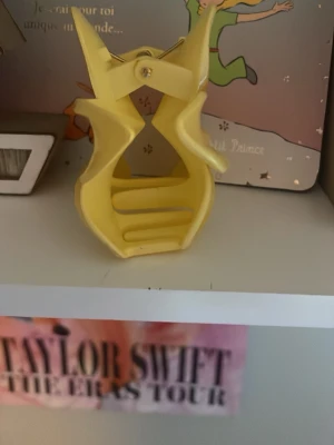 Gul hårklämma i blomform - Säljer en söt hårklämma i plast med blommig design och mjuk gul färg. Klämman har en unik form som liknar en blomma och är perfekt för att hålla upp håret på ett trendigt sätt. Enkel att använda och ger en snygg detalj till din frisyr.