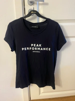 Svart Peak Performance t-shirt - Snygg svart t-shirt från Peak Performance med vit logga tryckt på bröstet. Klassisk rund halsringning och korta ärmar. Tillverkad i mjuk bomull som känns skön mot huden. Perfekt till jeans eller shorts för en clean och sportig look.