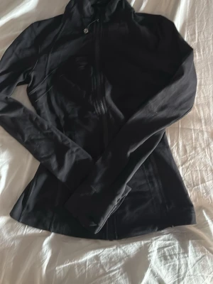 Svart träningsjacka från Lululemon - Snygg svart träningsjacka från Lululemon med figurnära passform, hög krage och dragkedja framtill. 