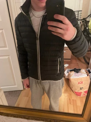 Svart dunjacka från Colmar - Säljer en svart/mörkgrön dunjacka från Colmar med quiltad design och silverfärgad dragkedja. Jackan har två fickor med dragkedja och en grön insida som ger en snygg kontrast. Perfekt för kalla vinterdagar och riktigt stilren look.