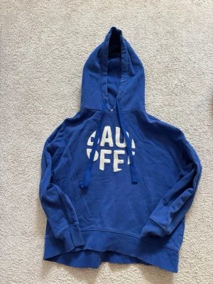 Blå hoodie med tryck och huva - Säljer en blå hoodie med stor huva och dragsnören. På bröstet står det 'BAD PFF' i vita, fluffiga bokstäver. Hoodien har ribbade muddar vid ärmar och nederkant. Perfekt för en chill och avslappnad stil.