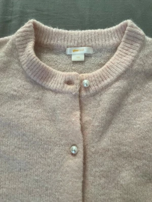 Ljusrosa kofta från Gina Tricot - Supersöt ljusrosa kofta från Gina Tricot med rund halsringning och pärlknappar framtill. Koftan är stickad i ett mjukt material och har långa ärmar samt ribbade muddar vid hals och ärmslut. Perfekt för lager på lager och en feminin touch storlek 170 men jag som är 17 år och är 167 lång passade mig bra som en 55 kg 