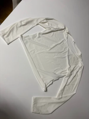 Vit  långärmad topp - Snygg vit mesh topp med lång ärm och rund halsringning. Tunn och lätt, perfekt att styla lager på lager eller bära som den är för en clean look. Enkel design utan mönster eller detaljer, vilket gör den superenkel att matcha med allt. I cut it wit sisors its univen at the bottom 