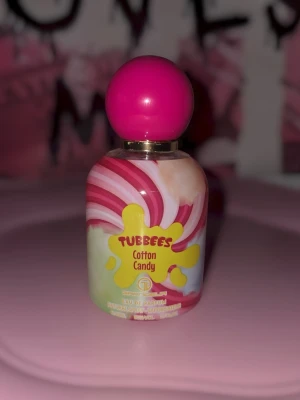 Tubbees Cotton Candy parfym - Säljer en Tubbees Cotton Candy parfym med färgglad swirl-design i rosa, vitt och gult. Flaskan har en rund form och ett klatschigt rosa lock. Doften är inspirerad av sockervadd och flaskan är tillverkad i glas med plastlock.