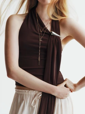 Brun topp med detaljer - Snygg brun topp med draperad detalj och metallspänne vid axeln. Toppen är ärmlös och har en asymmetrisk design som ger en cool och modern look. Tillverkad i mjukt, stretchigt material som sitter bekvämt mot kroppen.