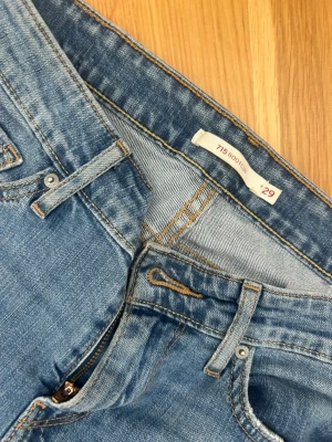 Levi's 715 Bootcut jeans ljusblå - Säljer ett par ljusblå Levi's 715 Bootcut jeans med klassisk femficksmodell och bootcut-ben. Jeansen har slitningar och en större reva på ena benet för en trendig look. Tillverkade i bomull med snygg tvätt och detaljerade sömmar. Säljer då jag ej använder!