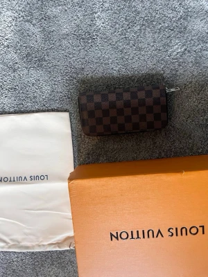  brun plånbok - Snygg brun plånbok. Plånboken har dragkedja runtom och är tillverkad i canvas med detaljer i läder. Kommer  ej med original ask och dustbag. Perfekt för dig som gillar lyxiga accessoarer.