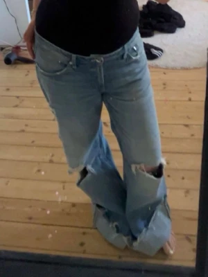 Baggy jeans - Säljer ett par ljusblå jeans med stora slitningar och hål på knäna samt råa kanter nertill. Perfekta för en avslappnad och trendig look. De sitter baggy.