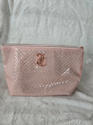 Glittrig rosa necessär från juicy Couture  - Säljer en glittrig rosa necessär från L'Oréal med ett snyggt mönster och ett metalliskt L'Oréal-emblem framtill. Väskan har dragkedja upptill och är perfekt för smink eller småprylar. Materialet är glansigt och ger ett lyxigt intryck.