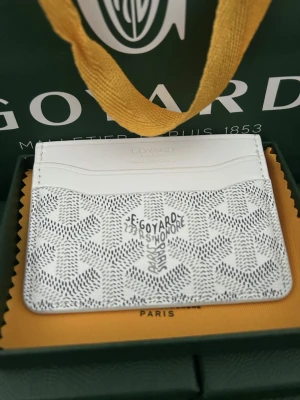 Plånbok Vit - Snyggt vitt kortfodral med det klassiska mönstret i grått och svart. Fodralet har flera kortfack och är tillverkat i exklusivt läder och canvas. Perfekt för dig som vill ha en stilren och lyxig accessoar i fickan.