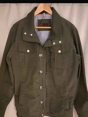 Mörkgrön overshirt med fickor - Stilren mörkgrön overshirt från Dressman med två bröstfickor med tryckknappar och två sidofickor. Overshirten har knappstängning framtill och en hög krage. Materialet är slitstarkt och passar perfekt till lager-på-lager-stil.