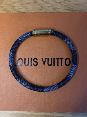 Armband L - Snyggt armband från LV i blått och svart flätat material med guldfärgat magnetlås. Armbandet har en modern och stilren design med diskret LV-logga på låset. Perfekt accessoar för dig som gillar exklusiva detaljer.