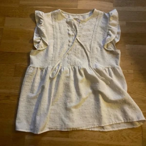 Vit blus med volangärmar - Söt vit blus med broderade detaljer och volangärmar. Blusen har knytband fram och ett lätt strukturerat tyg med små prickar.  