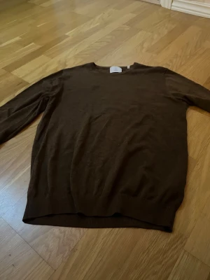 Brun stickad tröja från Bläck - Mysig brun stickad tröja från Bläck i storlek M. Tröjan har rund halsringning, långa ärmar och ribbade muddar vid ärmslut och nederkant. Perfekt för lager på lager och enkel att matcha med jeans eller chinos.