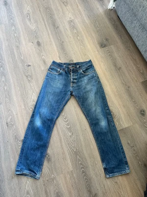 Blå raka jeans från nudie - Klassiska blå jeans från Wrangler med rak passform och fem fickor. Jeansen har en snygg tvätt med lätt slitna detaljer och läderpatch bak i midjan. Perfekta för en avslappnad och stilren look.