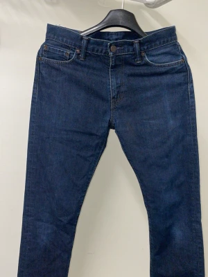 Mörkblå Levi's jeans straight fit - Säljer ett par klassiska mörkblå jeans från Levi's med rak passform. Jeansen har fem fickor, gylf med dragkedja och knapp samt den ikoniska läderpatchen bak i midjan. Tillverkade i slitstark denim som passar perfekt till alla tillfällen.
