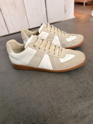 Maison margiela gats - Snygga sneakers i beige mocka och vitt läder med klassisk gummisula. Skorna har en låg profil och stilrena linjer som passar till det mesta. Perfekta för dig som gillar minimalistisk och clean stil.