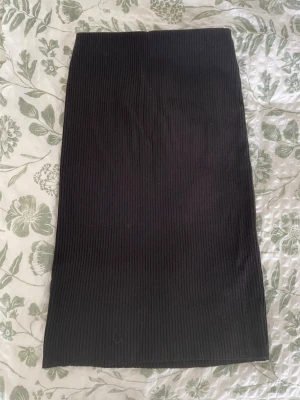 Svart ribbad kjol - Säljer en svart ribbad kjol från H&M i storlek M. Kjolen är stretchig och går ner till vaderna och är i mycket bra skick. 