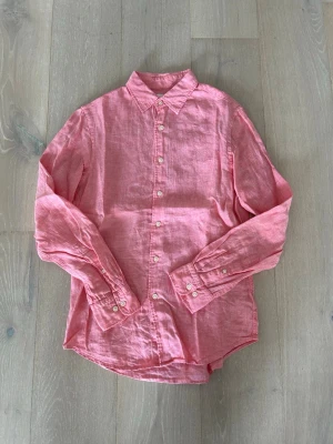 Linneskjorta från Uniqlo - Säljer en snygg rosa skjorta från Uniqlo i luftigt linne. Skjortan har klassisk krage, långa ärmar och knappar framtill samt vid ärmsluten. Perfekt för dig som gillar en avslappnad men stilren look.