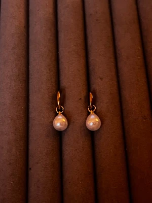 Guldiga örhängen med droppformade pärlor - Säljer ett par stilrena örhängen med guldfärgade ringar och droppformade vita pärlor. Örhängena har en klassisk design som känns både trendig och tidlös. Perfekta för dig som gillar en elegant touch till din look.