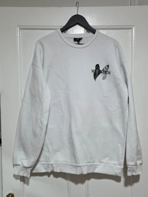 Vit sweatshirt Mutation tryck - Säljer en vit sweatshirt från SMOG med svart tryck av en fjärilsvinge på ryggen och en på bröstet. Stort 'MUTATION'-tryck på ryggen och coolt motiv nedtill. Tröjan har rund hals och långa ärmar. Perfekt för dig som gillar streetwear och unika prints.