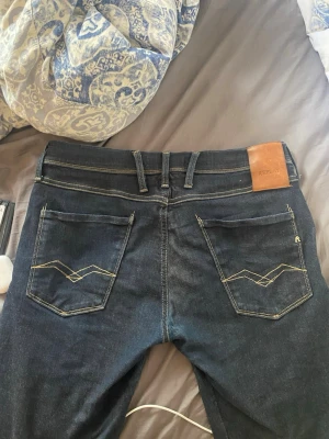 Mörkblå jeans från Replay - Snygga mörkblå jeans från Replay med klassisk femficksdesign och kontrastsömmar. Bakfickorna har unika broderade detaljer och ett läderpatch med logga i midjan. Perfekta för dig som vill ha stilrena jeans med coola detaljer.