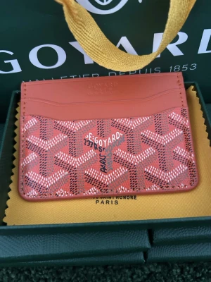 Plånbok orange - Snyggt rött kortfodral med det klassiska vita och svarta mönstret. Fodralet har flera kortfack och är tillverkat i läder och canvas. Perfekt för dig som vill ha en exklusiv och stilren accessoar i fickan.