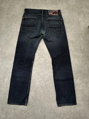 Salvage jeans från RRL Ralph Lauren - Snygga mörkblå jeans från RRL Ralph Lauren med raka ben och klassiska bakfickor. Jeansens patch har amerikansk flagga och broderad logga. Tillverkade i slitstark denim med coola detaljer och snygga slitage. Mått: Längd 101cm, Midja 41cm, Benöppningen 20cm