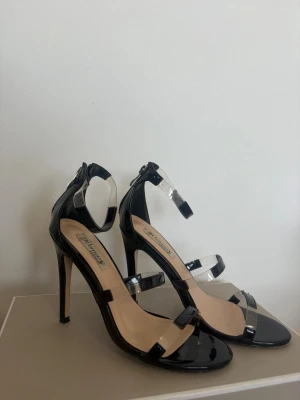 4 pumps i lack - Två par svarta lackpumps med transparenta remmar och smal klack, samt ett par klassiska röda och gråa lackpumps med spetsig tå och hög klack. Båda paren har en elegant och trendig design som passar till många olika looks. 