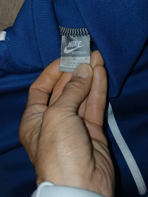 Blå Nike loungewear set - Snyggt blått loungewear set från Nike med dragkedja på tröjan och vita detaljer längs dragkedja och byxben. Setet har två fickor med dragkedja på tröjan och dragsko i midjan på byxorna. Perfekt för chill dagar hemma eller när du vill vara bekväm.