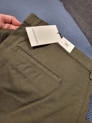Olivgröna chinos från These Glory Days 56 Xl - Snygga olivgröna chinos från These Glory Days med klassisk rak passform. Byxorna har två sidofickor, en bakficka och bälteshällor. Tillverkade i ett mjukt och slitstarkt bomullstyg som ger en clean och stilren look.